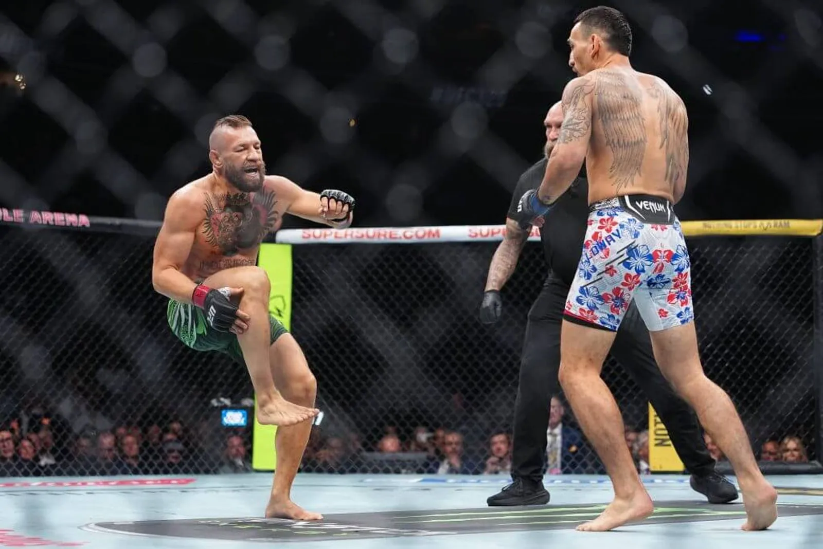 Conor McGregor, left, reacts in pain after suffering a leg injury before his bout versus Max Holloway.