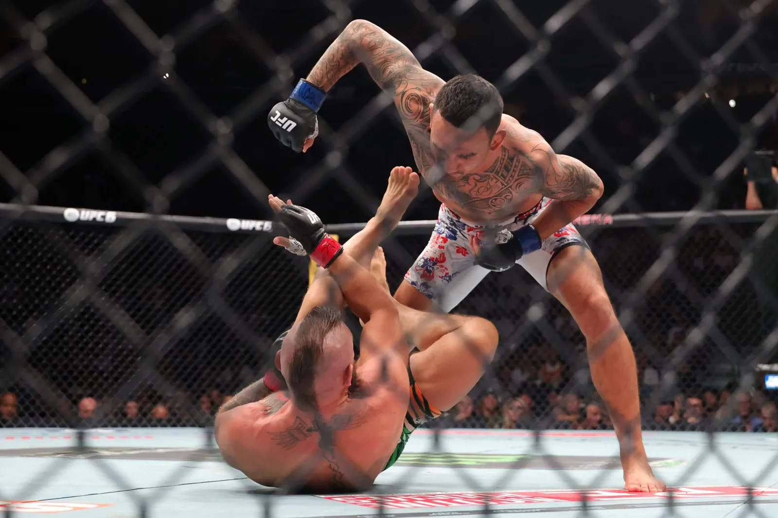 Conor McGregor, on the mat, tries to fend off Max Holloway, who is on his feet and punching down with his right hand.