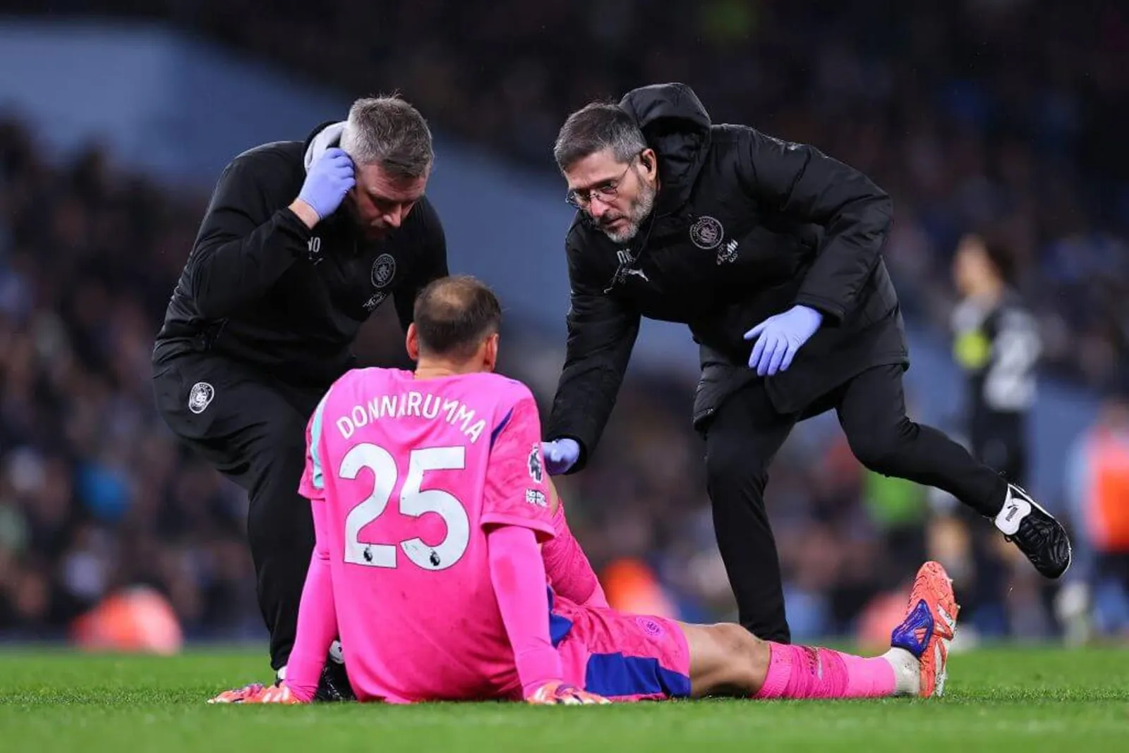 Gianluigi Donnarumma of Manchester City, wearing an all pink kit, receives treatment from two physios.