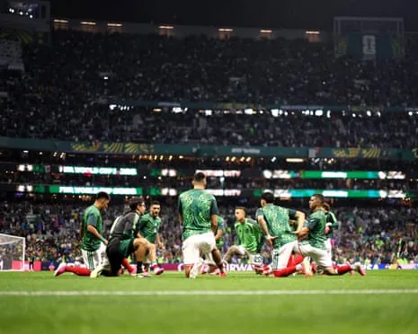 Mexico players in green patterned jerseys stretch and warm up on a pitch in a packed stadium